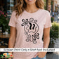 A woman wearing a light pink t-shirt with a black dripping smiley face graphic, set against a blurred outdoor cafe background. A white banner at the bottom reads 'Screen Print Only • Shirt Not Included'.