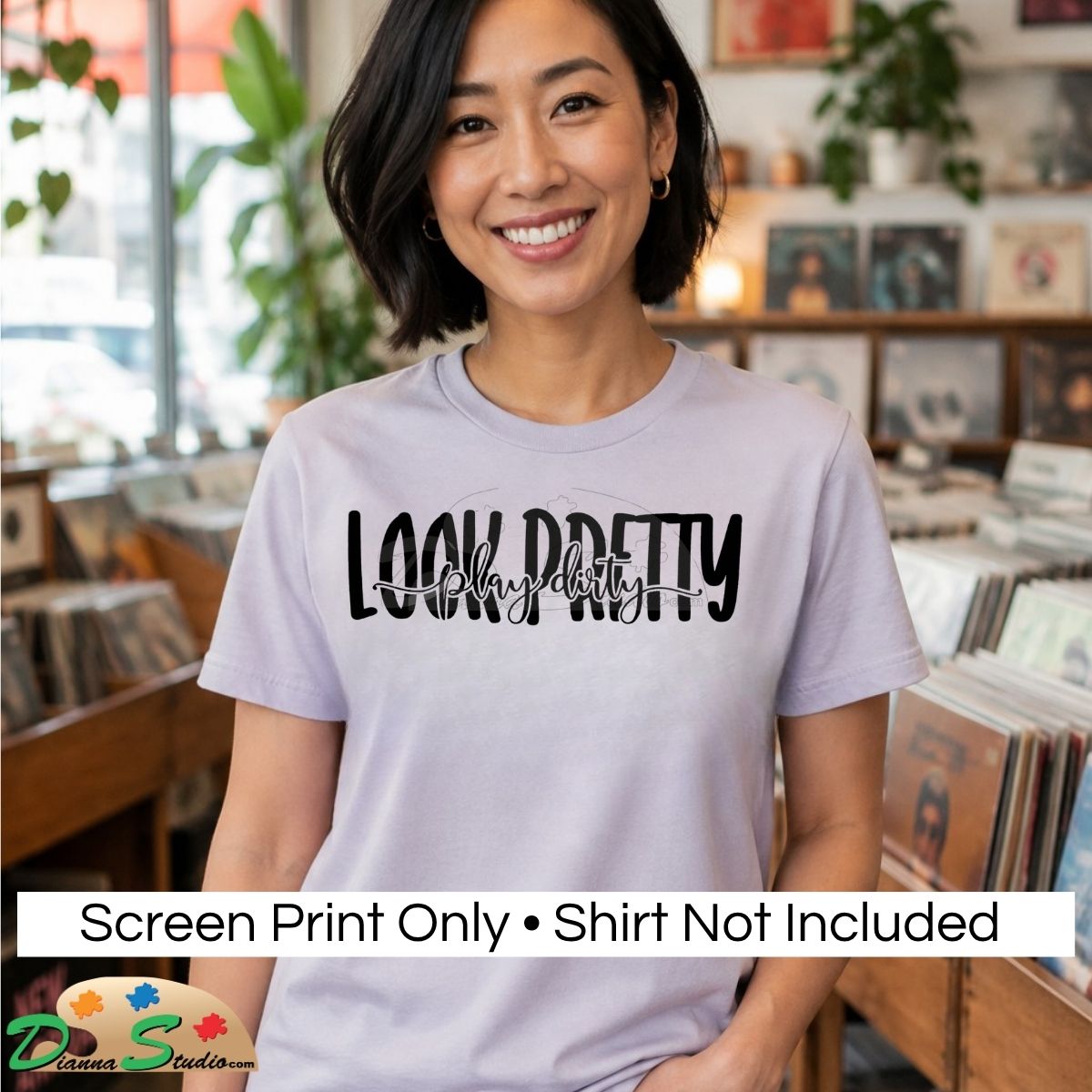 A smiling woman stands in a record store wearing a light lavender-gray t-shirt with a black screen-printed graphic that reads 'LOOK PRETTY' and 'Play Dirty' in script on top. A white banner at the bottom reads 'Screen Print Only • Shirt Not Included' and shows the 'DiannaStudio' logo.