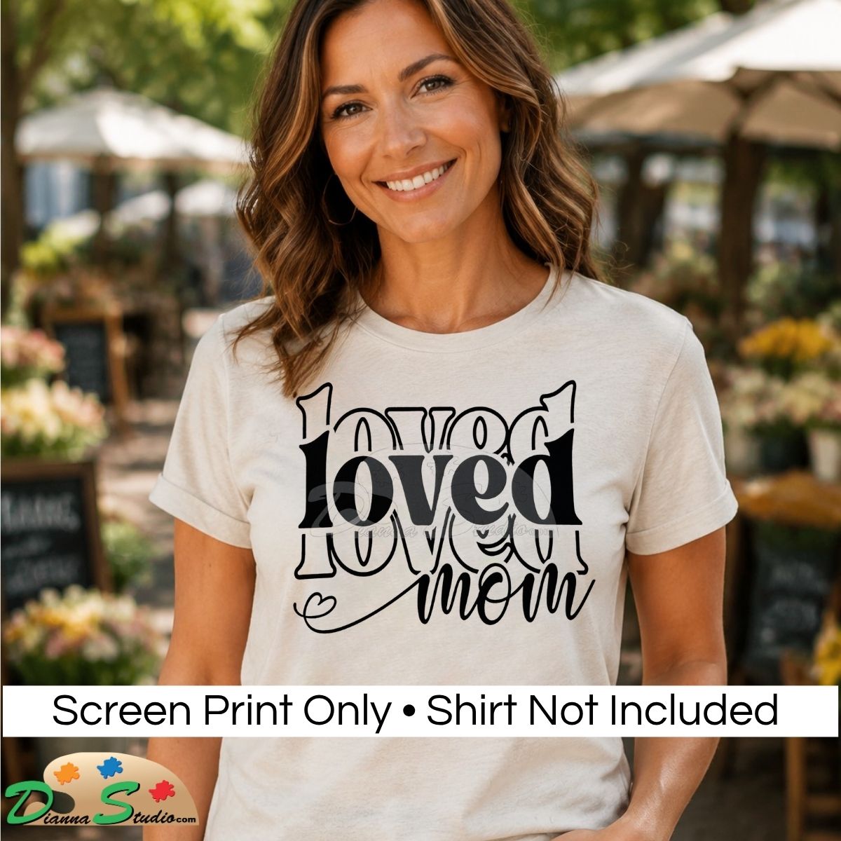 A woman wearing a light beige graphic t-shirt with the words 'loved mom' printed in black. The background is a blurred outdoor patio setting.