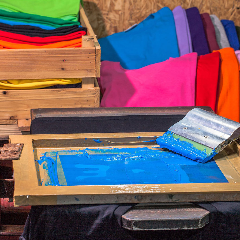 Blue screen printing ink and colorful shirts prepared for custom apparel printing.