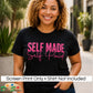 A smiling woman with curly hair wears a black graphic T-shirt with the words 'SELF MADE Self Paid' in hot pink lettering. The photo is taken outdoors with blurred plants and buildings in the background, and a white banner at the bottom reads 'Screen Print Only • Shirt Not Included' with a 'DiannaStudio' logo.