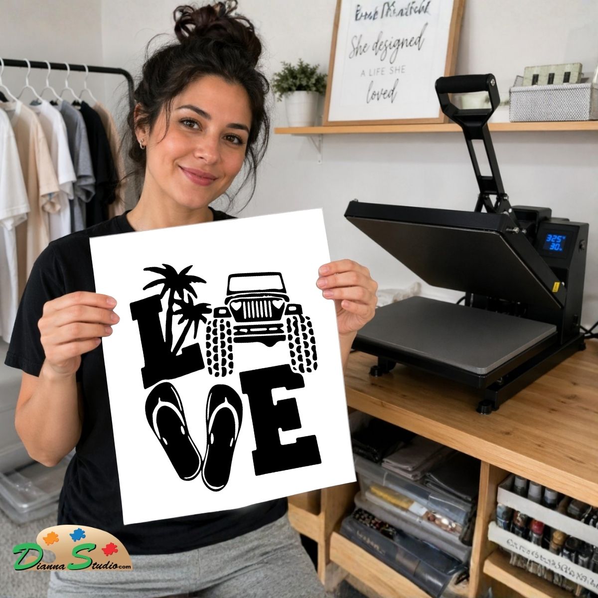 A woman holds up a white graphic print featuring the word 'LOVE' in black block letters, with a palm tree, Jeep Wrangler, and flip-flops. In the background, a black heat press machine sits on a wooden desk next to a clothing rack.