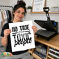A woman holds up a white square print with the text 'NO TIME for TOXIC people' in black lettering. She is standing in a craft room with a heat press machine on a wooden table behind her.