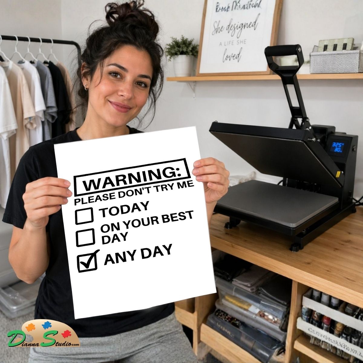 A woman holds up a white printed warning sign that reads 'WARNING: PLEASE DON'T TRY ME' with checkboxes for today, on your best day, and any day. She is standing in a craft room with a heat press machine on a wooden table behind her.