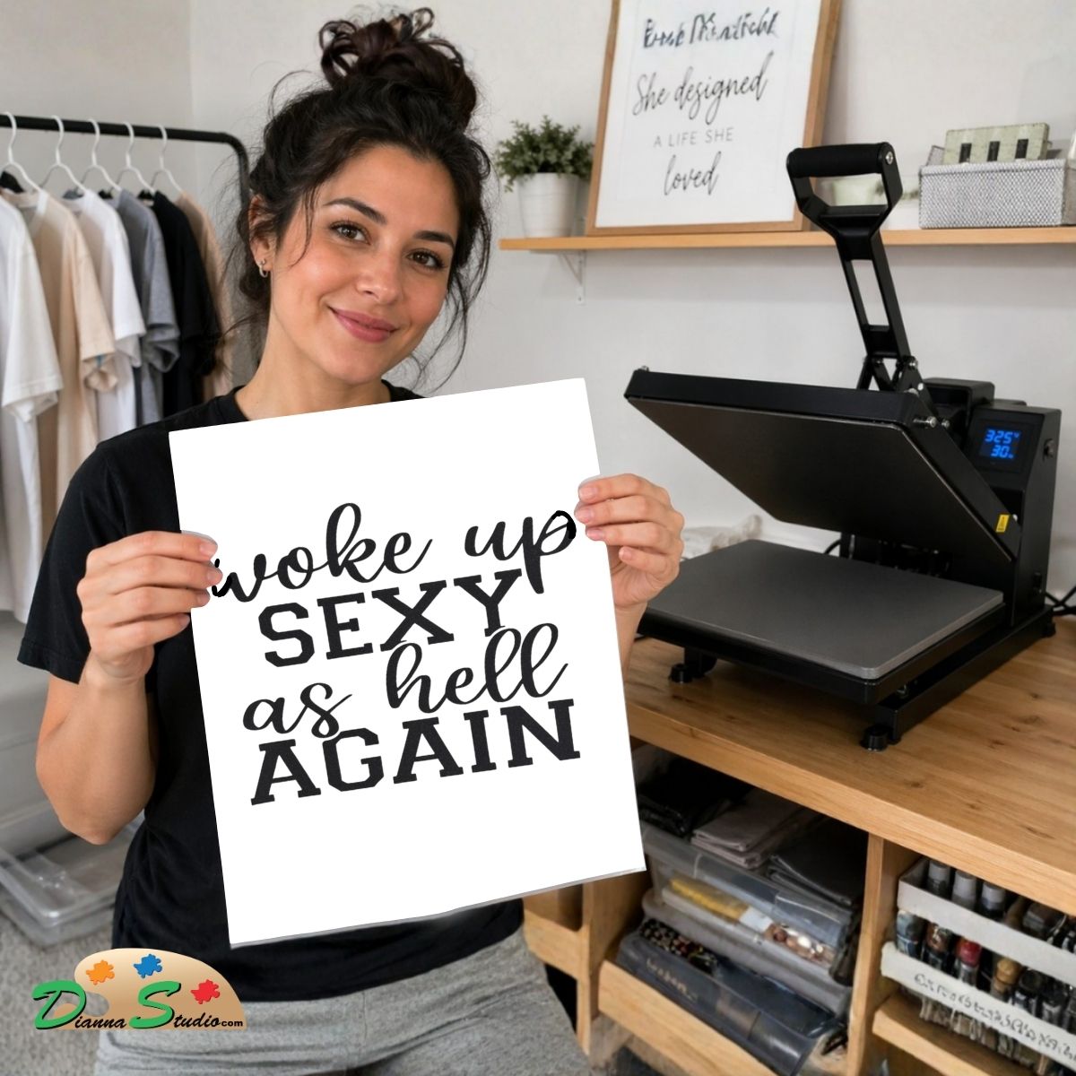 A woman holds up a white square print with black text reading 'woke up SEXY as hell AGAIN' in a craft room setting, with a heat press machine on a wooden table behind her.
